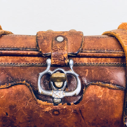 Closeup of vintage brown leather handbag with metal clasp, showing worn and weathered texture in a rustic, bohemian style reminiscent of 1960s fashion.