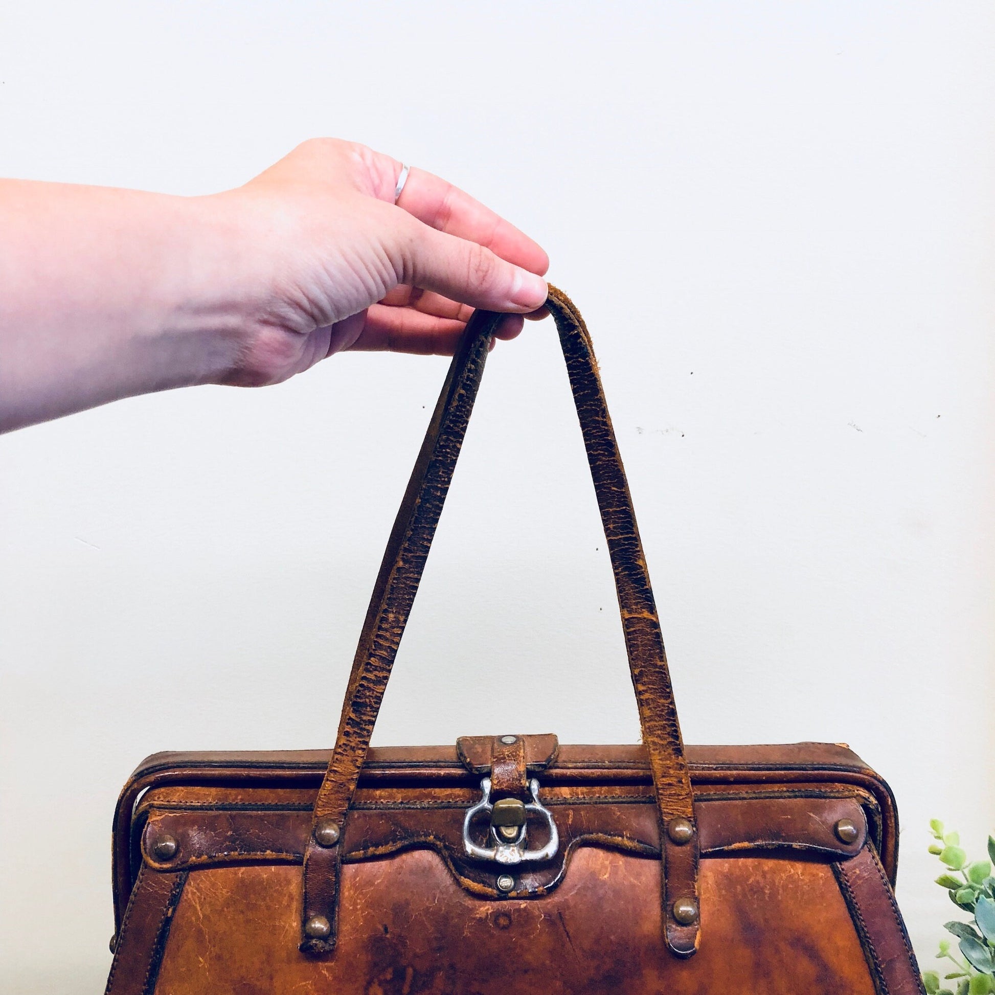 Vintage brown leather handbag held by hand, showing ornate stitching and metal accents in a bohemian 1960s style.