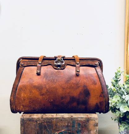 Vintage brown leather handbag with rustic, bohemian style from the 1960s, sitting on a wooden trunk next to a vase of white flowers