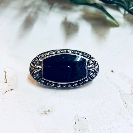 Vintage Art Deco style sterling silver brooch with black onyx and marcasite detailing on a white background.