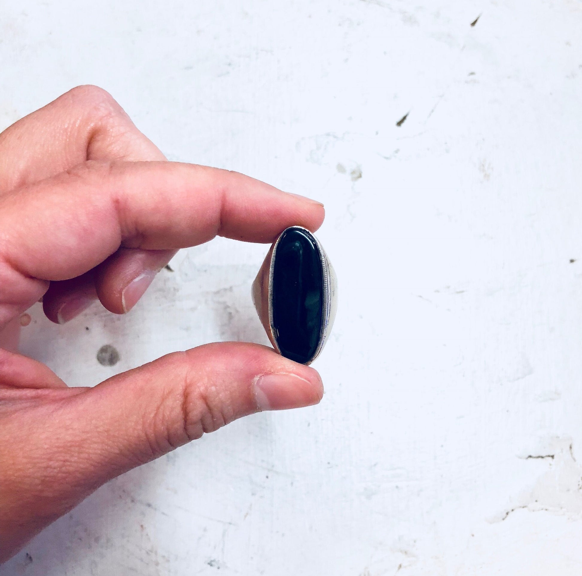 Hands holding a vintage sterling silver cocktail ring featuring a large, elongated black onyx stone against a white background.