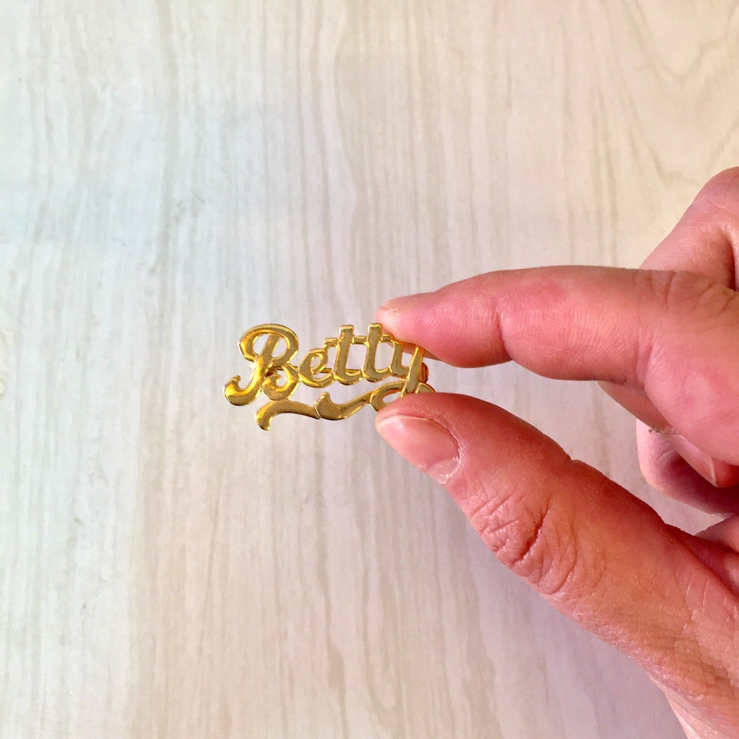 Vintage gold "Betty" nameplate brooch held in fingers against wooden background