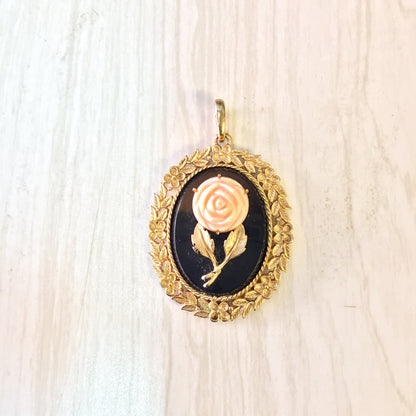 Vintage gold-toned cameo pendant featuring a pink rose on a black background, surrounded by an ornate floral frame