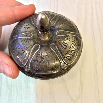 Antique sterling silver and ebony spinning top toy by Gorham with fortune-telling messages engraved on the sides, held in a hand against a light wood background.