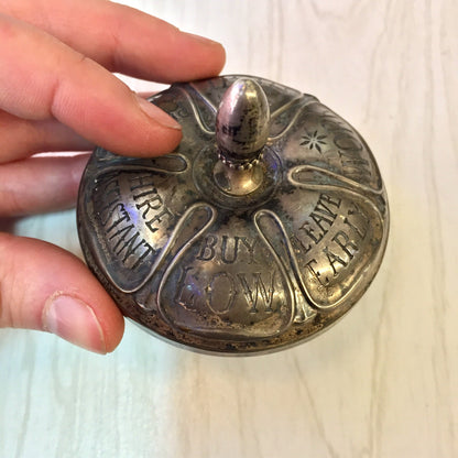 Antique sterling silver and ebony spinning top toy by Gorham with engraved text that reads "Ask It Re: Real Estate" held in a person's hand.