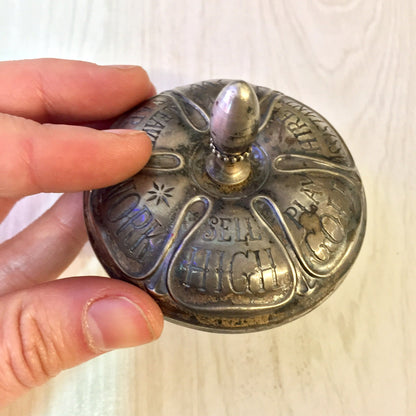 Antique sterling silver spinning top toy with ebony handle and engraved text "SETA HIGH", held in a person's fingers.