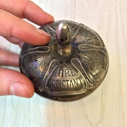 Antique sterling silver and ebony spinning top toy by Gorham, engraved with "Fire Assistant" and various firefighting symbols, held in someone's hand.