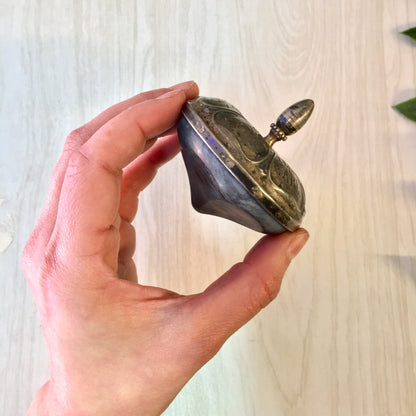 A hand holding an antique sterling silver and ebony spinning top toy made by Gorham