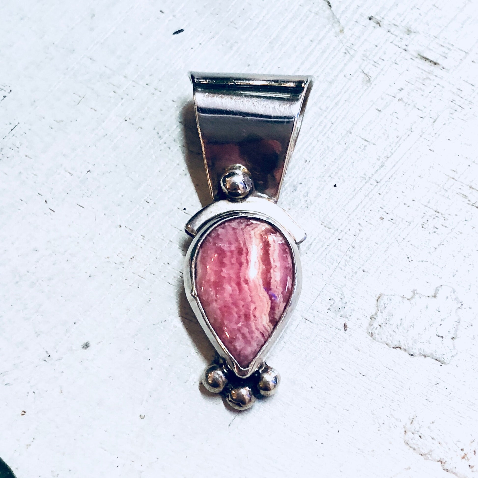 Vintage sterling silver pendant with pear-shaped pink rhodochrosite gemstone on a textured white background.