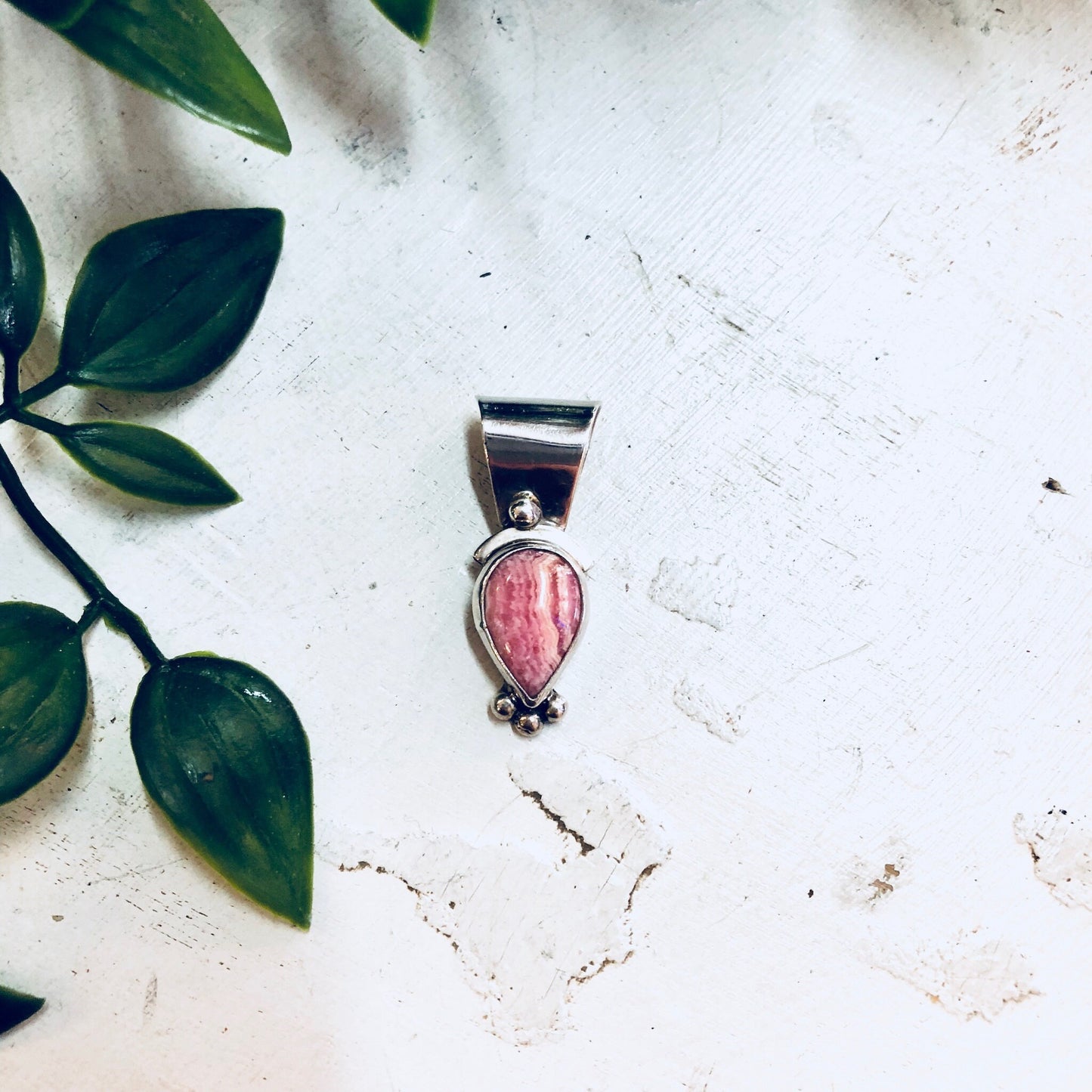 Vintage sterling silver pendant with pink rhodochrosite gemstone on white textured background with green leaves