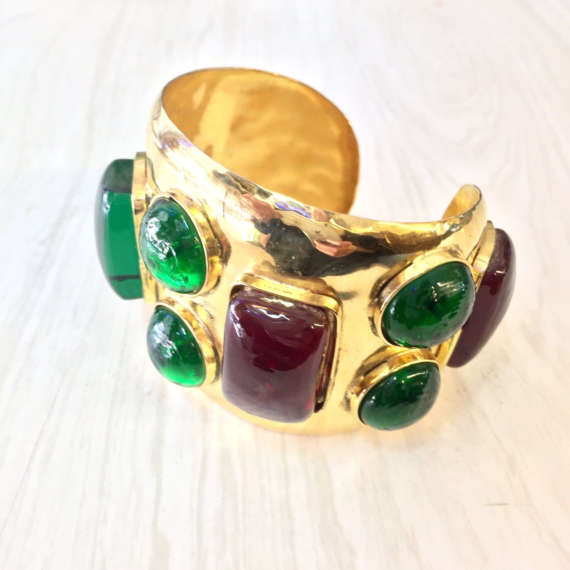 Gold toned vintage cuff bracelet with red and green gemstone-like beads, creating a bold and colorful statement piece of jewelry.