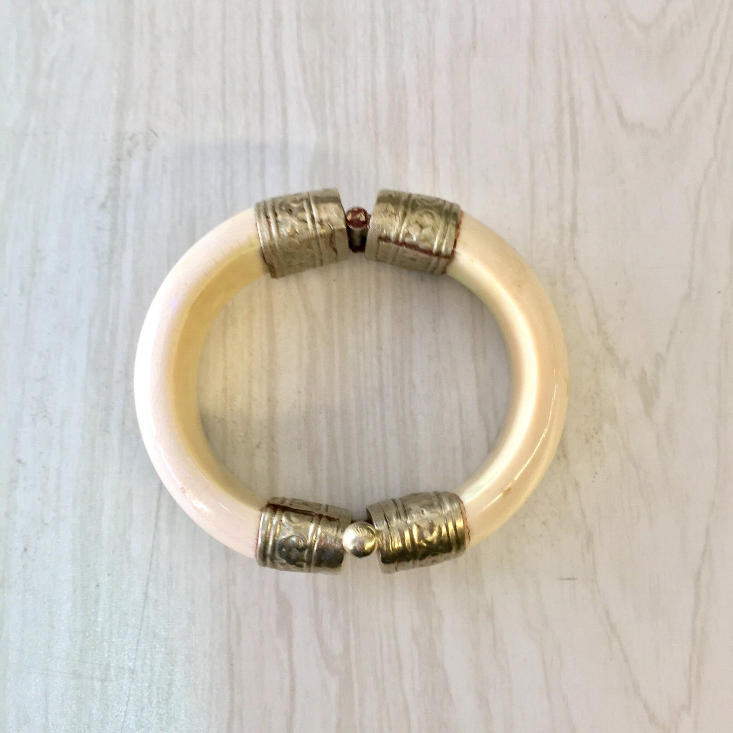 Vintage white and silver tone hinged bangle bracelet with intricate engraved metal beads and pin closure, photographed on light wood surface.