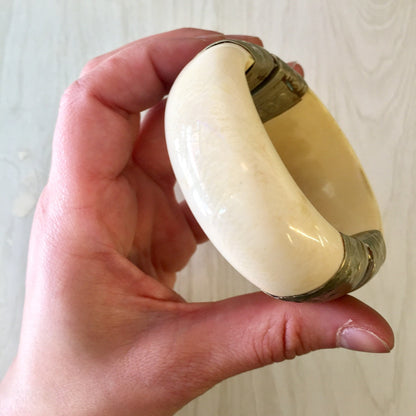 Vintage white and silver hinged bangle bracelet held in hand, showing large size and pin closure clasp against light background.