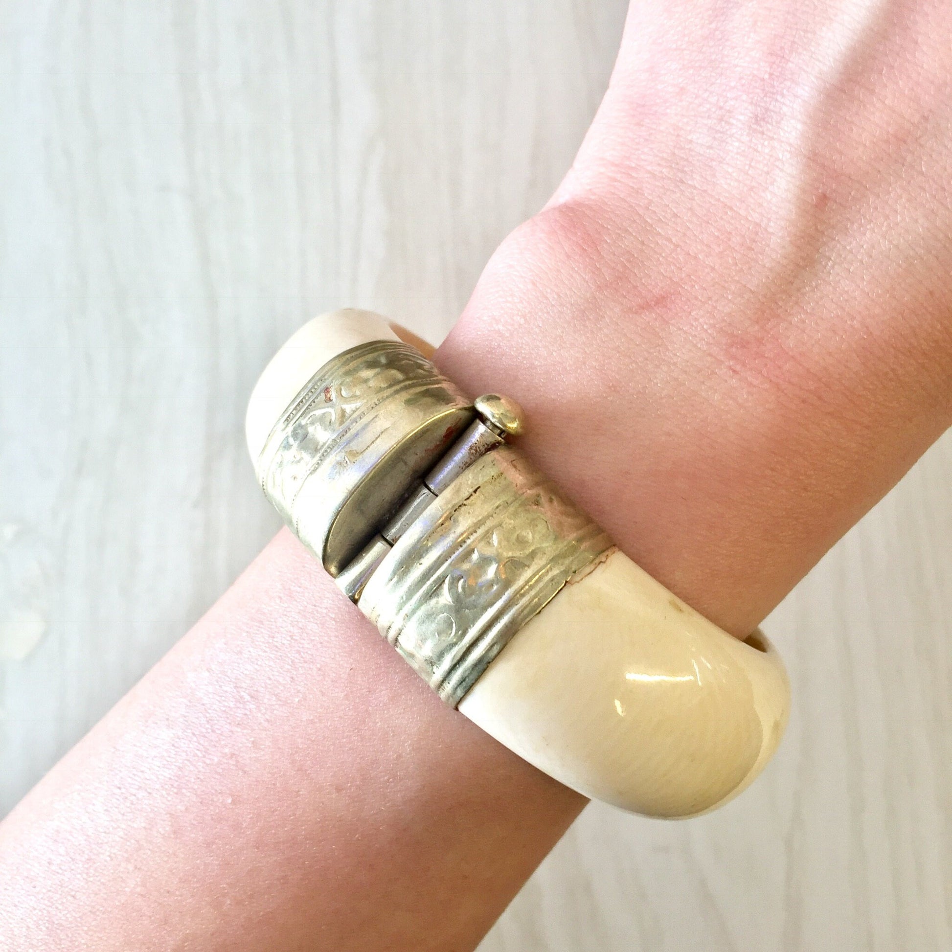 Vintage white and silver tone hinged bangle bracelet with pin closure, shown worn on a wrist.