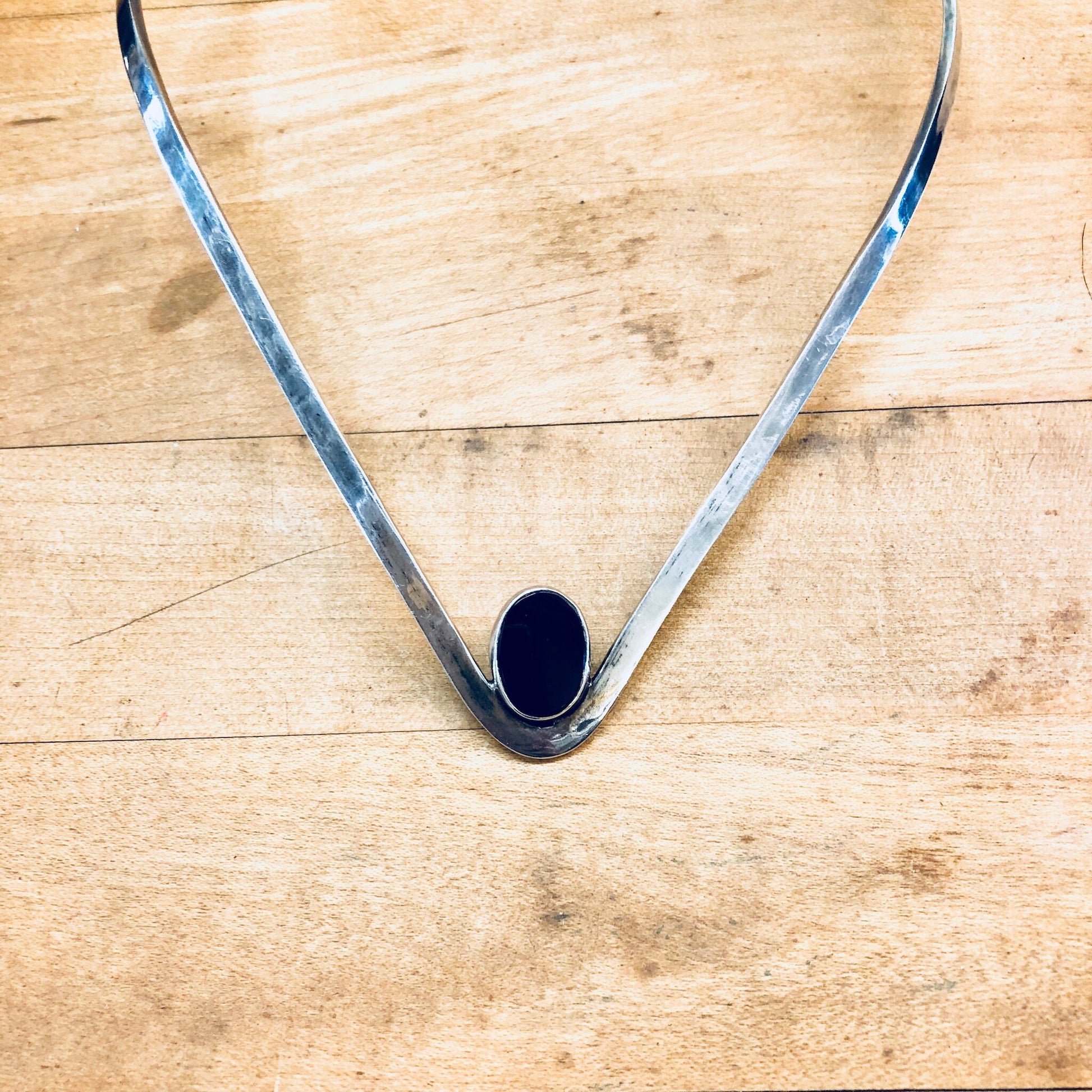 Vintage sterling silver choker necklace with black onyx center stone, forming a V-shaped collar design against a wooden background.