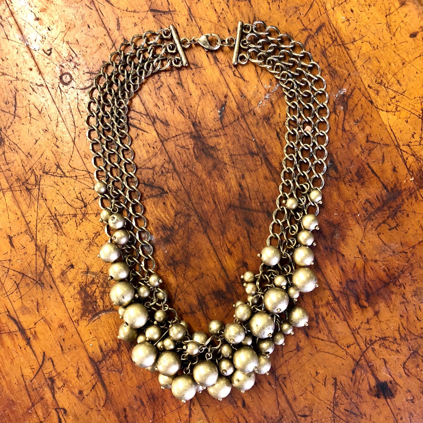 Vintage brass-toned choker necklace with multiple chains and dangling pearl-like beads, laid flat on a scratched wooden surface.