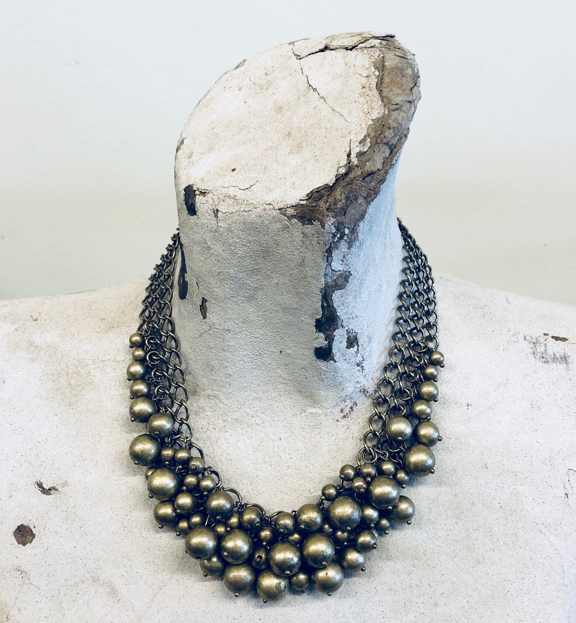 Vintage brass-toned bib necklace with multiple strands of spherical beads draped on weathered concrete surface