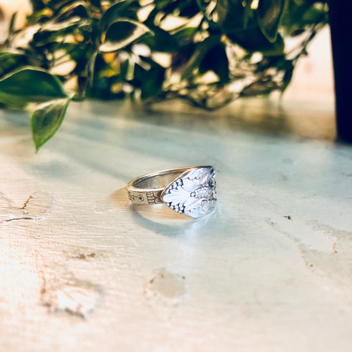 Vintage silver spoon ring with floral design on a rustic wooden surface near green foliage