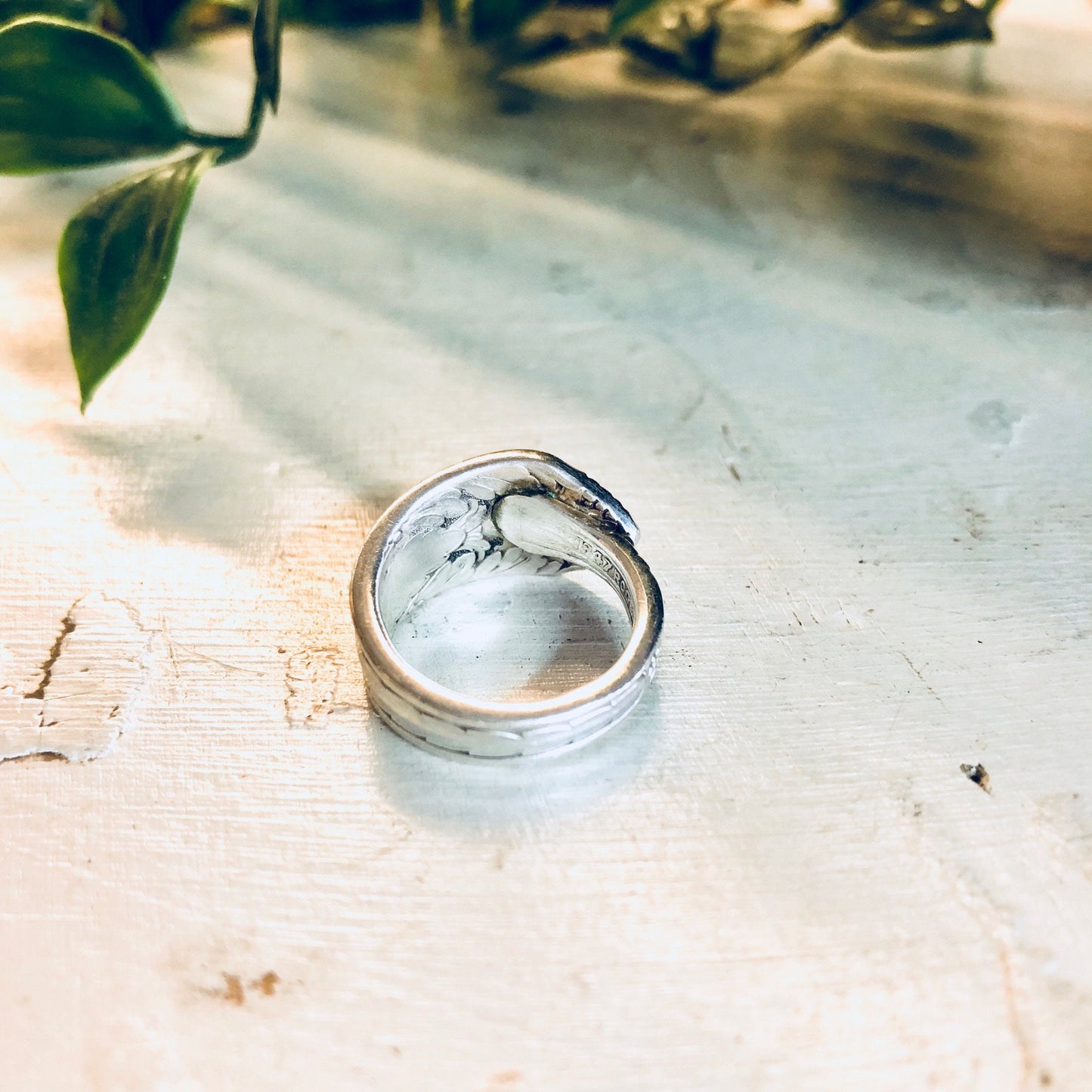 Vintage silver spoon ring with floral design on weathered wooden surface next to green leaves