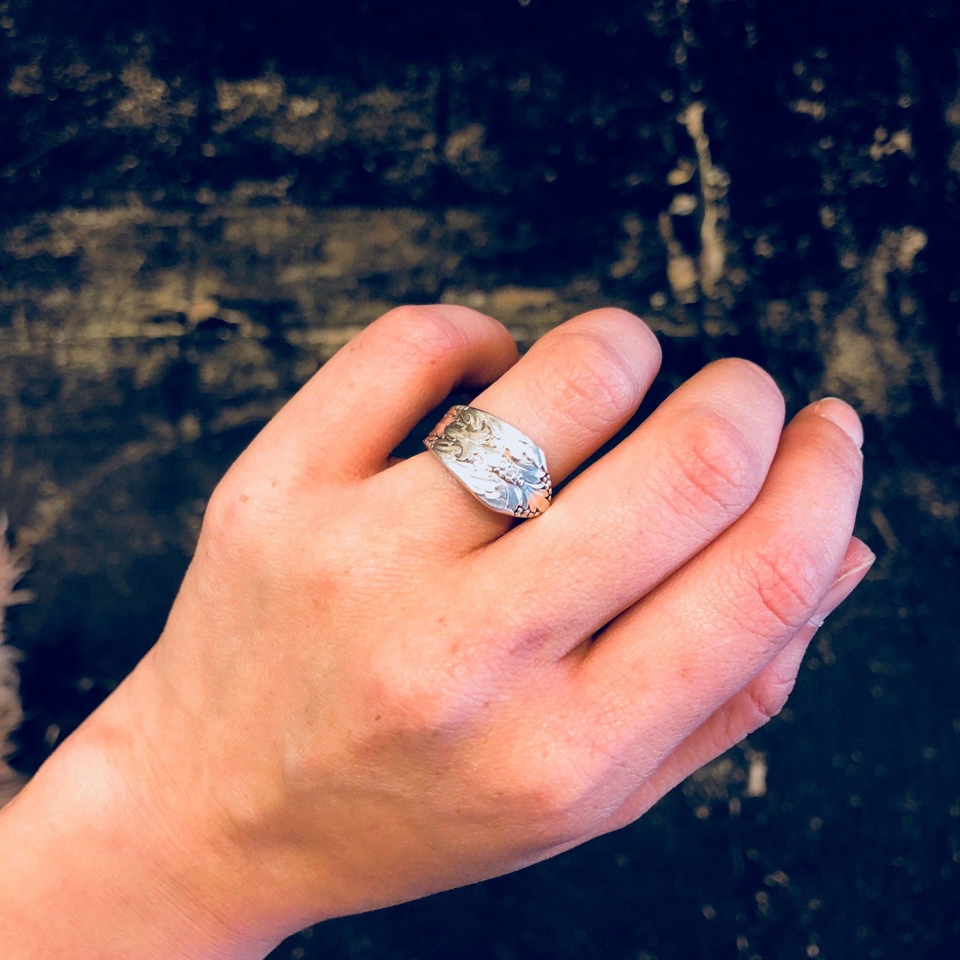 Vintage silver spoon ring with floral design, worn on hand against dark textured background