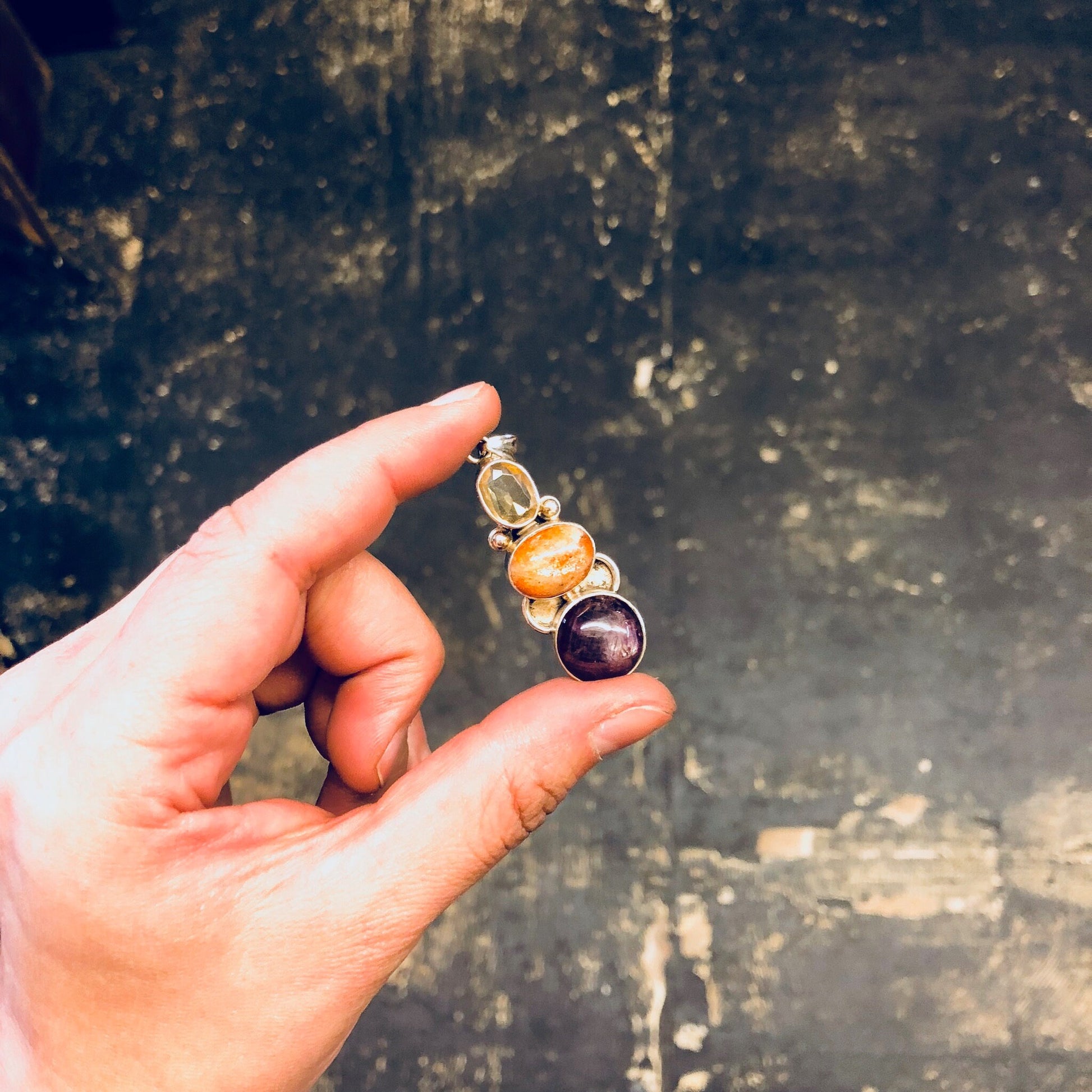 Vintage sterling silver pendant necklace with smoky quartz, orange, and purple natural stones held in hand against textured dark background