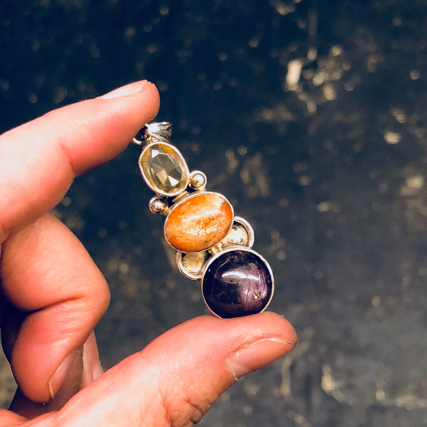 Vintage silver pendant with natural smoky quartz, orange, and purple stones held in a hand, showcasing the intricate design and colorful gemstones of the sterling silver necklace against a dark background.