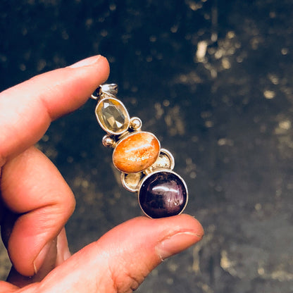 Vintage silver pendant with natural smoky quartz, orange, and purple stones held in a hand, showcasing the intricate design and colorful gemstones of the sterling silver necklace against a dark background.