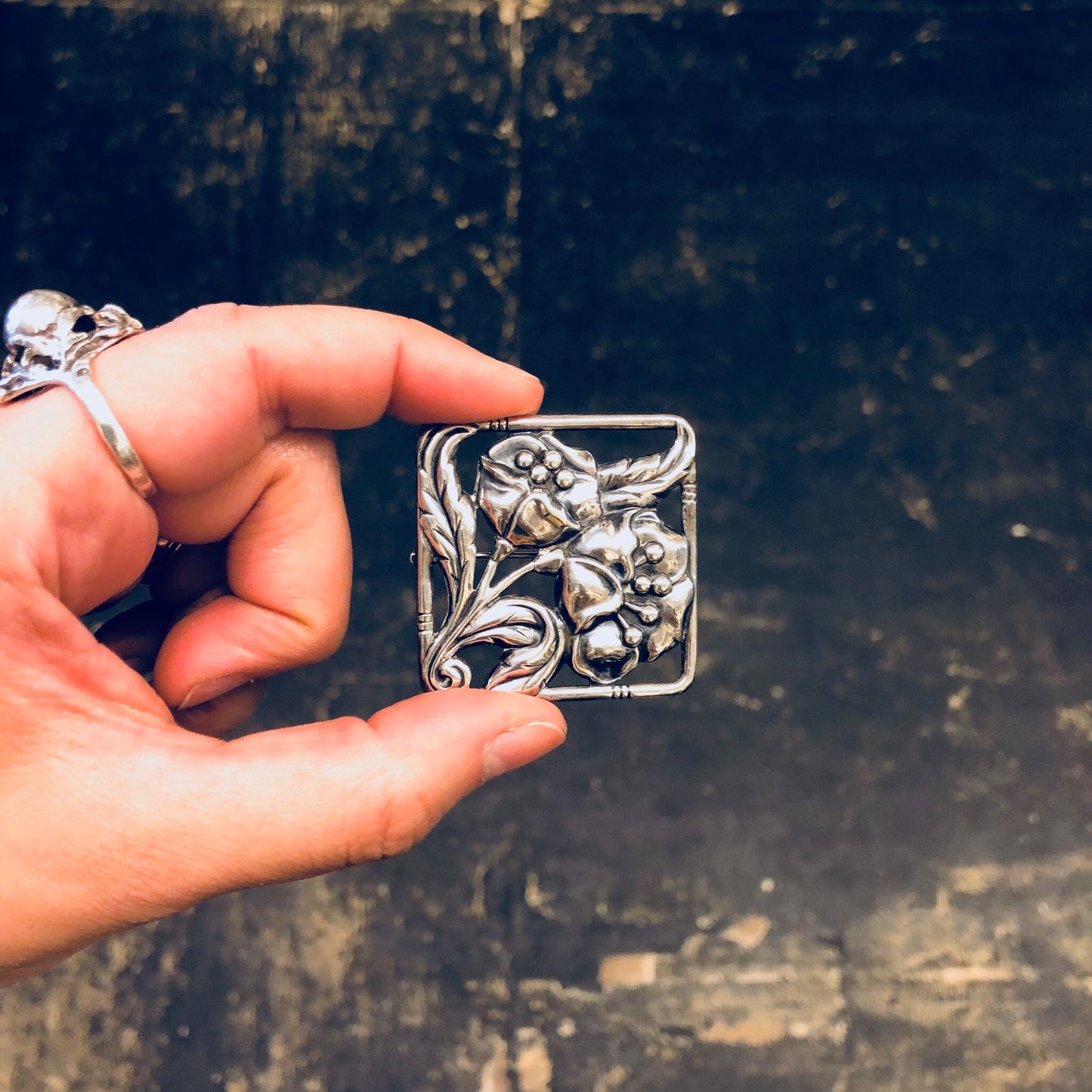 Vintage Dancraft sterling silver floral brooch from the 1940s, held in hand against a worn, textured background.