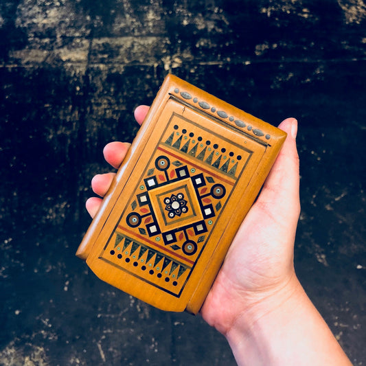 Vintage wooden cigarette case with intricate geometric inlaid design held in hand against dark background