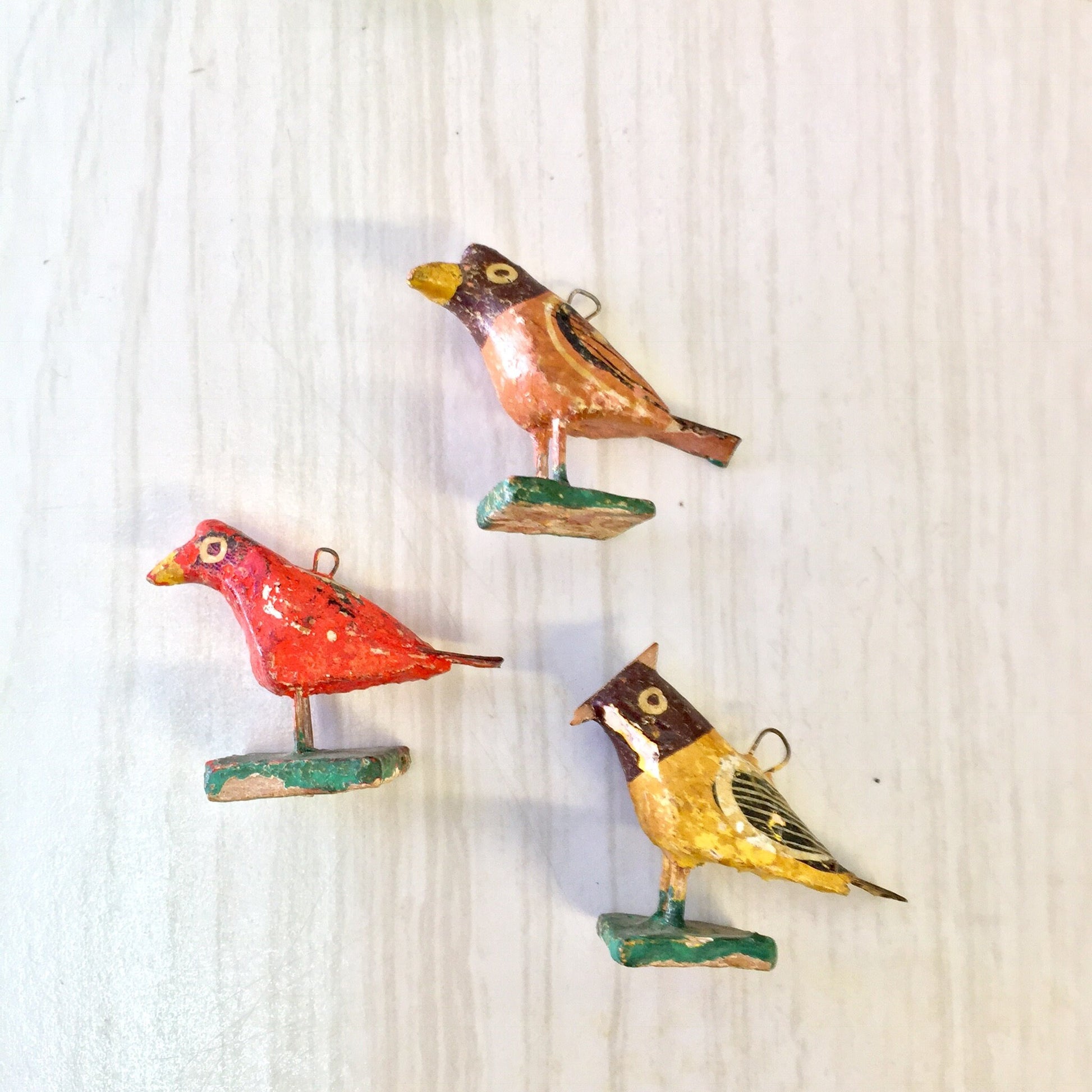 Colorful paper mache bird beads for jewelry making and crafts in red, blue, yellow, and brown tones on a light wood background.