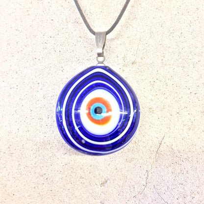 Blue evil eye glass pendant necklace with concentric rings of white, blue and red on silver chain against textured off-white background