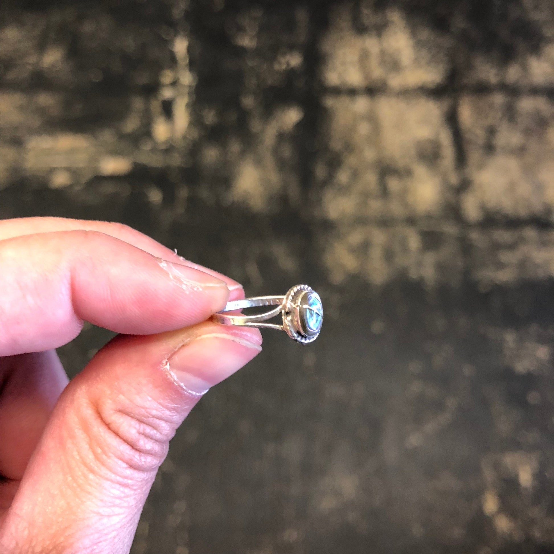 Vintage sterling silver ring with small abalone shell inlay, held between fingers against a weathered wooden background.