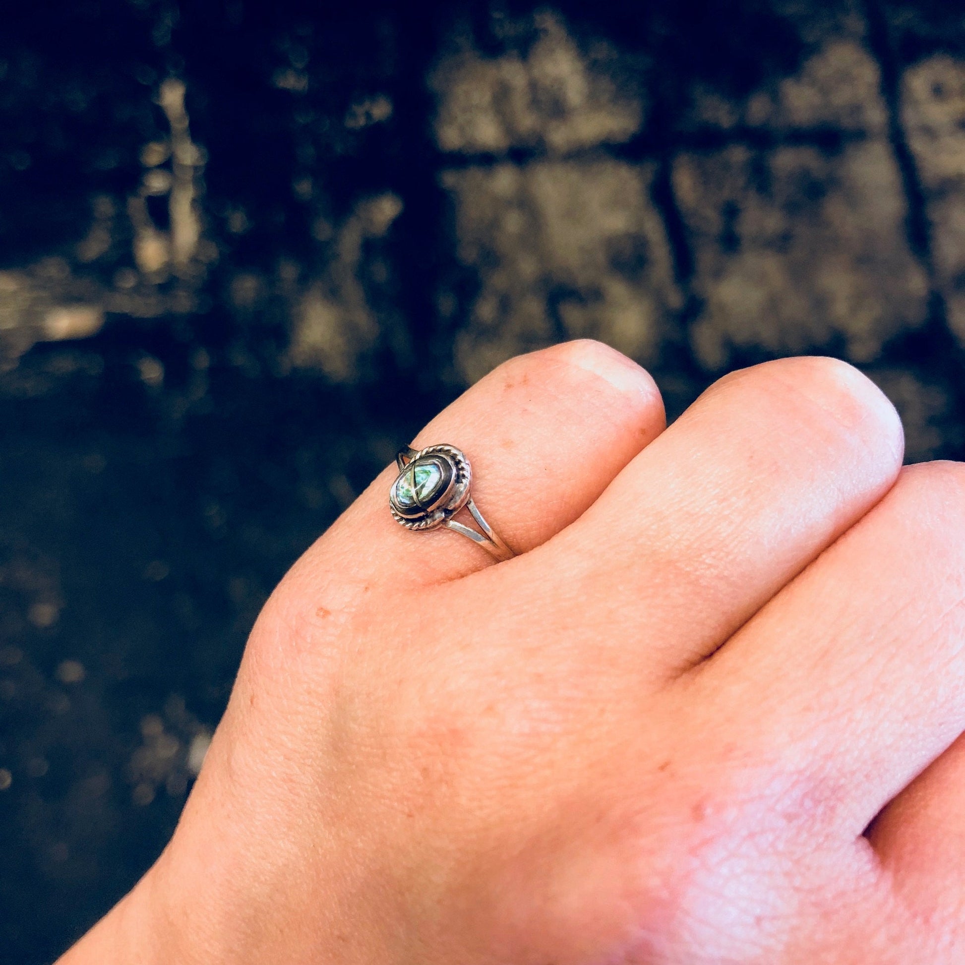 Vintage sterling silver ring with oval abalone shell inlay, worn on pinky finger against dark textured background.