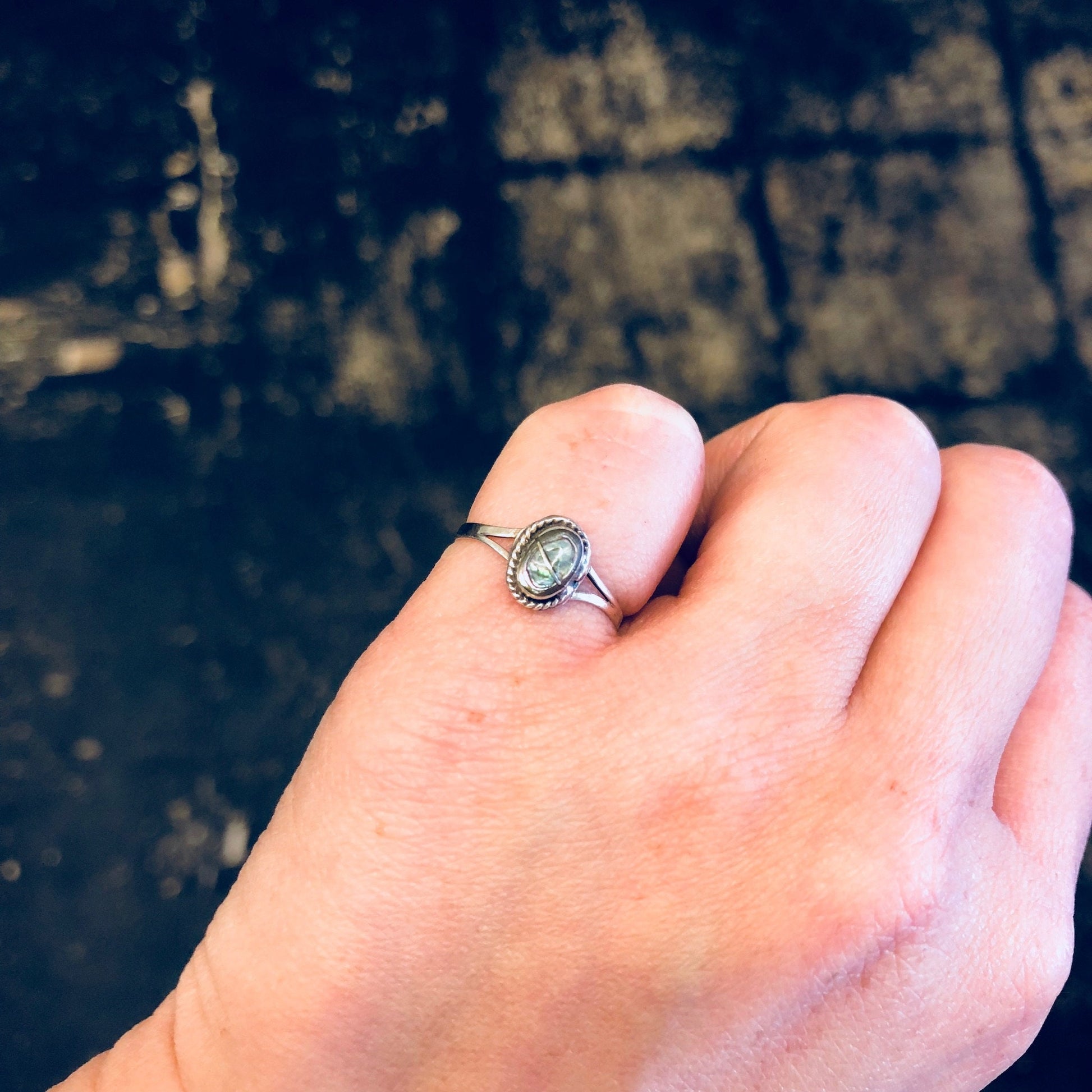 Vintage sterling silver abalone shell pinky ring on hand against dark background