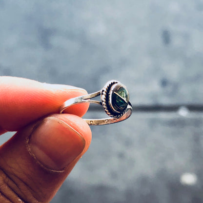 Vintage sterling silver pinky ring with abalone shell inlay, held between fingers against blurred background