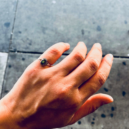 The image shows a person's hand wearing a small vintage silver ring with an abalone shell inlay. The ring is worn on the pinky finger and the abalone shell has an iridescent blue sheen against the silver metal band.