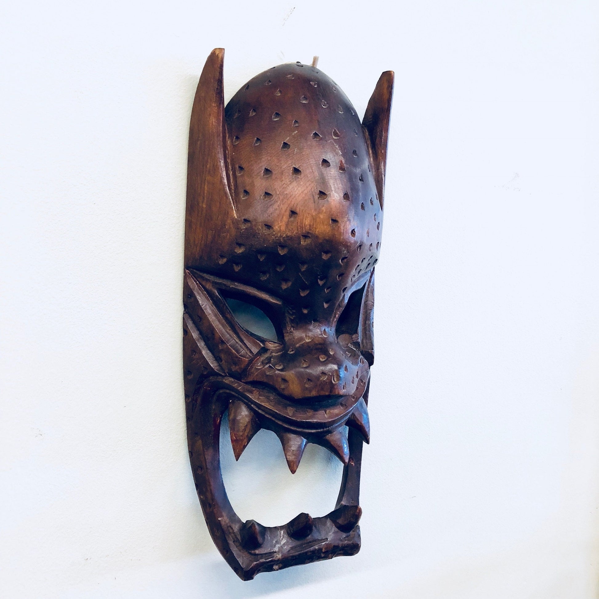 Vintage hand carved wooden mask with intricate dot patterns and jagged teeth, displayed as a wall hanging for primitive home decor.