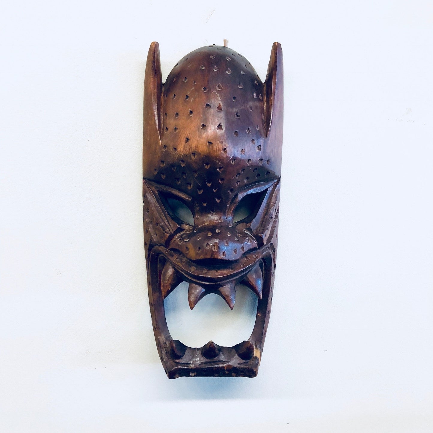 Vintage hand carved wooden mask with intricate details and brown finish, suitable for primitive wall decor or hanging display in the home.