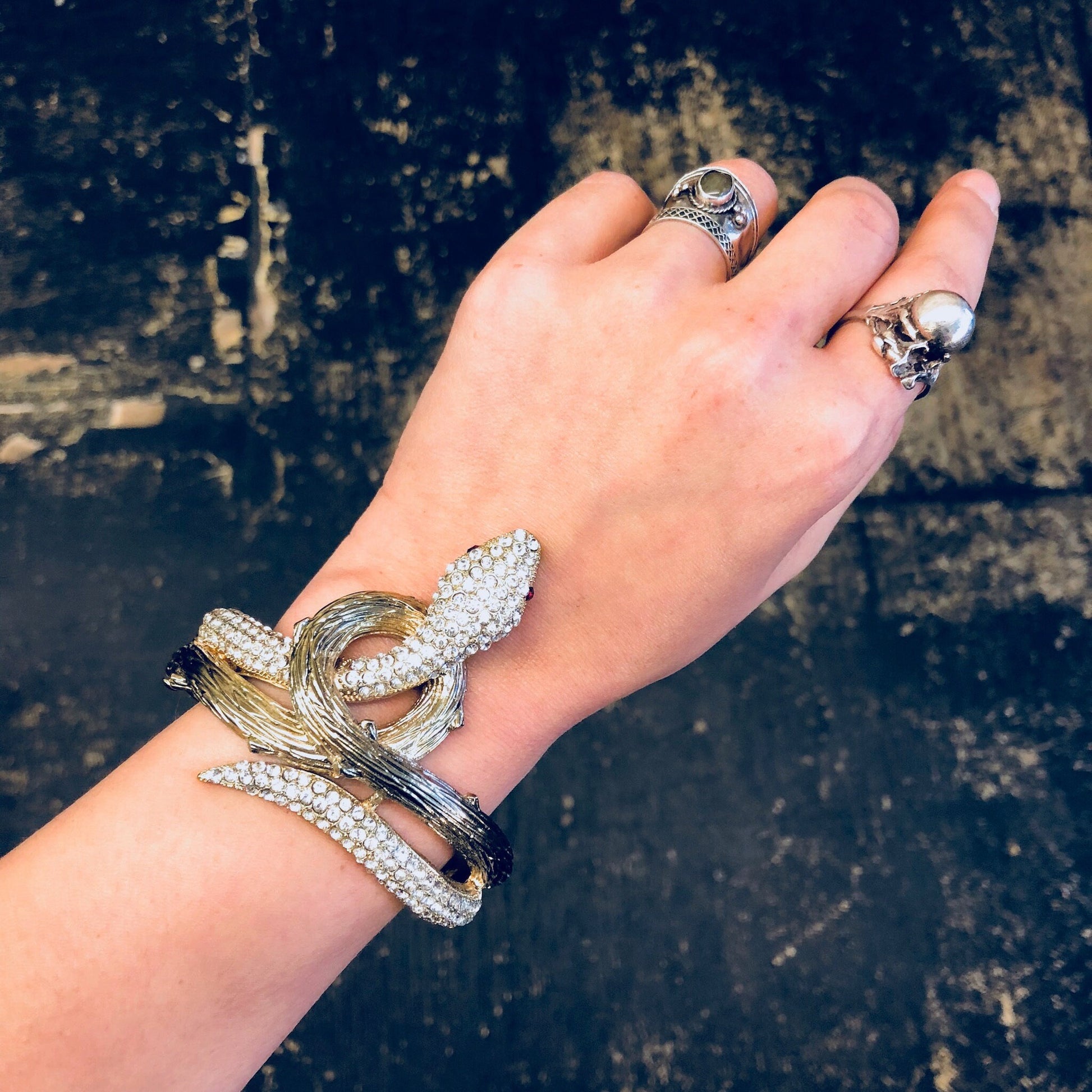 Vintage snake bracelet with rhinestones on a wrist, gold toned hinged cuff jewelry against weathered wooden background