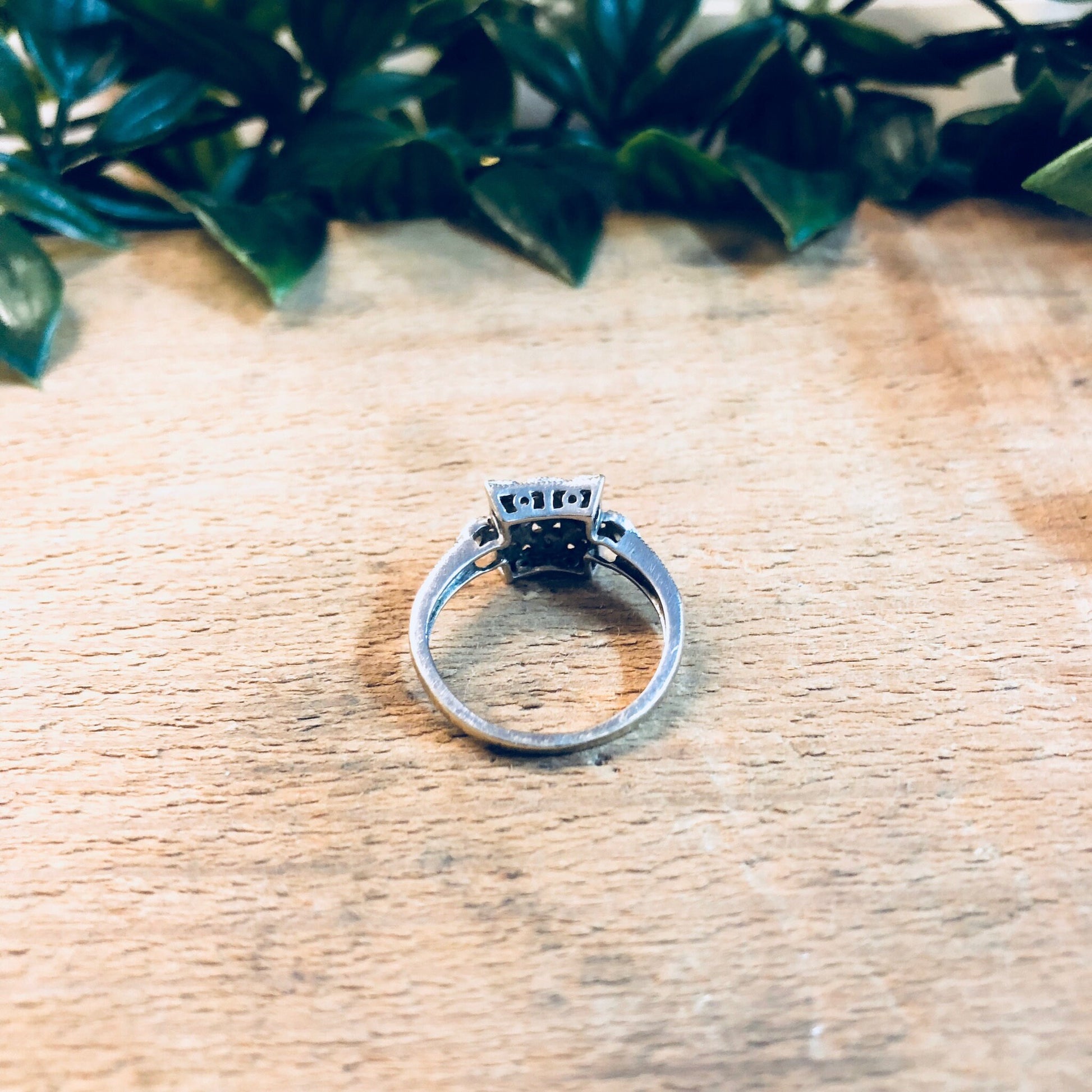 Vintage 14K white gold art deco diamond engagement ring on wooden surface with greenery in background