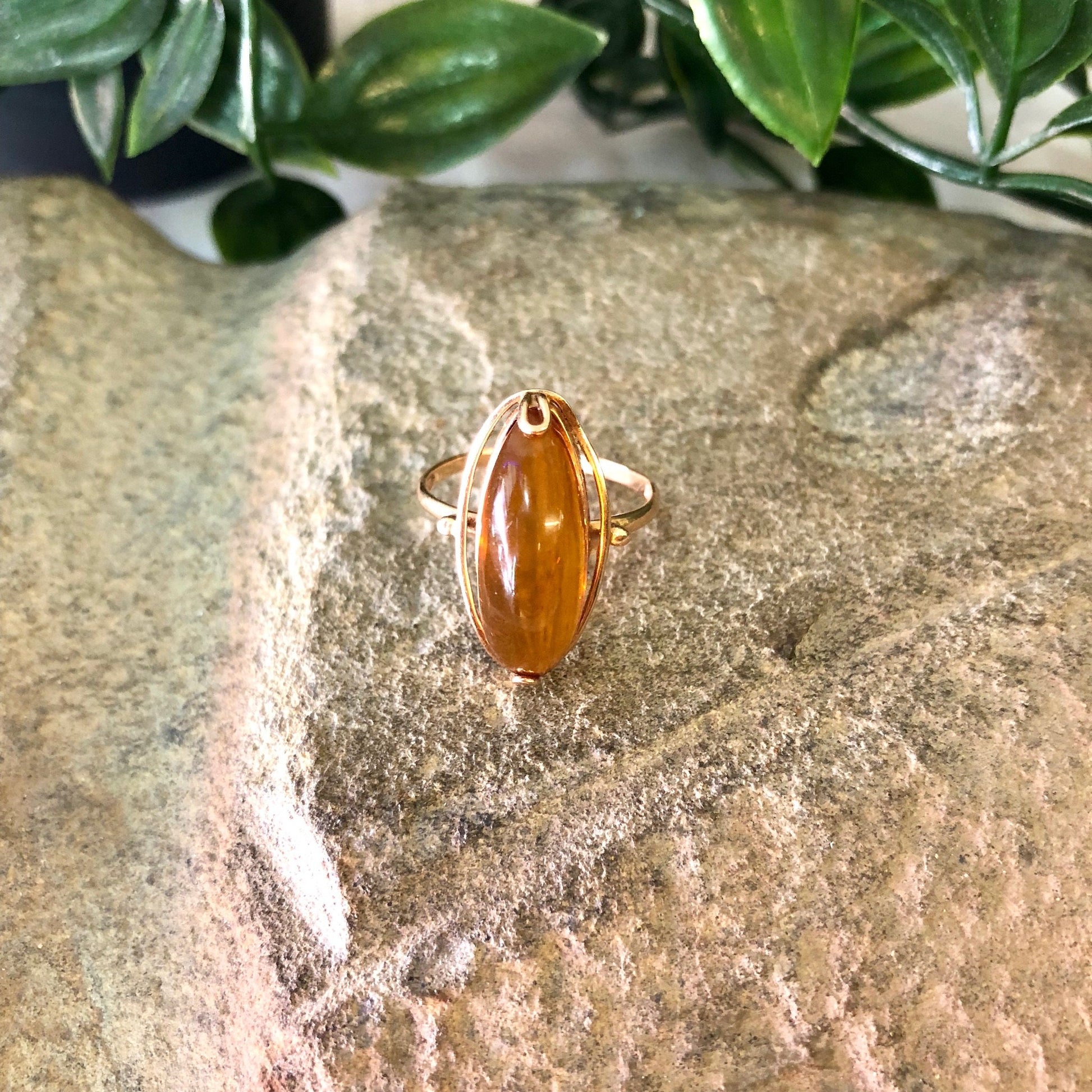 Vintage 10K yellow gold ring with oval amber stone on textured gold background surrounded by green leaves