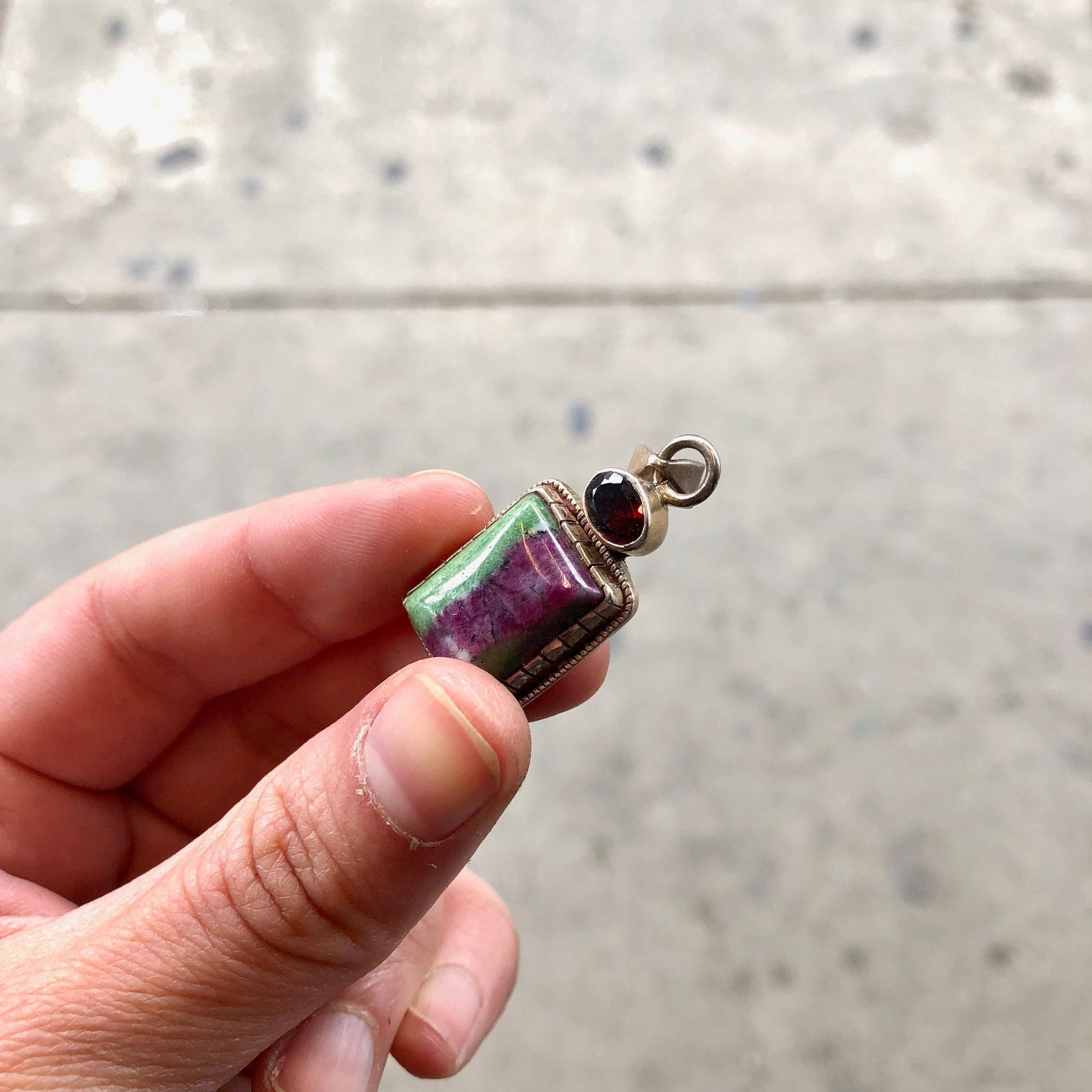 Vintage sterling silver pendant with green, purple and red natural stone accents, held in a hand against a grey textured background.