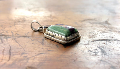 Vintage silver pendant with green and purple natural stone accents on a weathered wooden surface