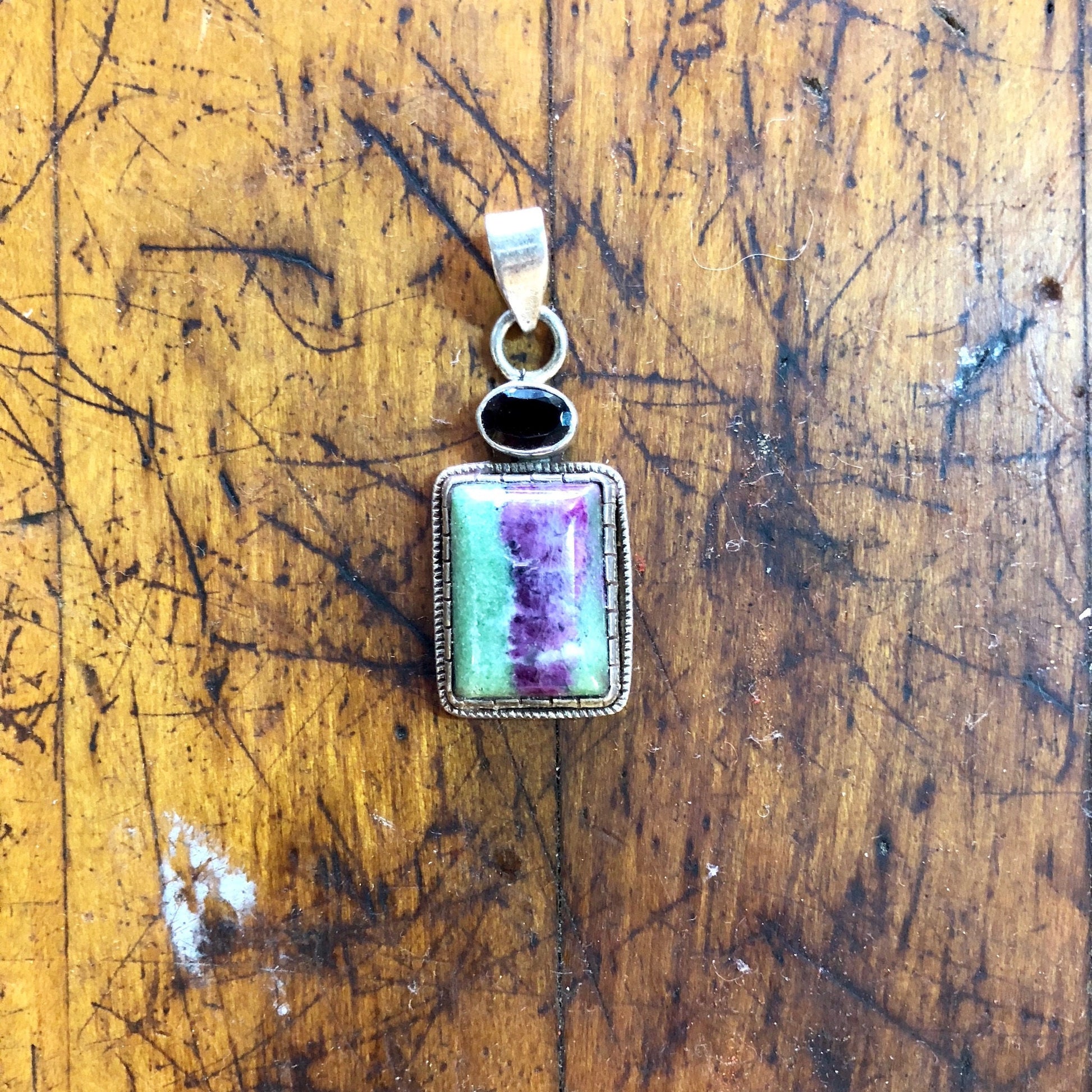 Vintage sterling silver pendant with green and purple natural stone on a wood surface