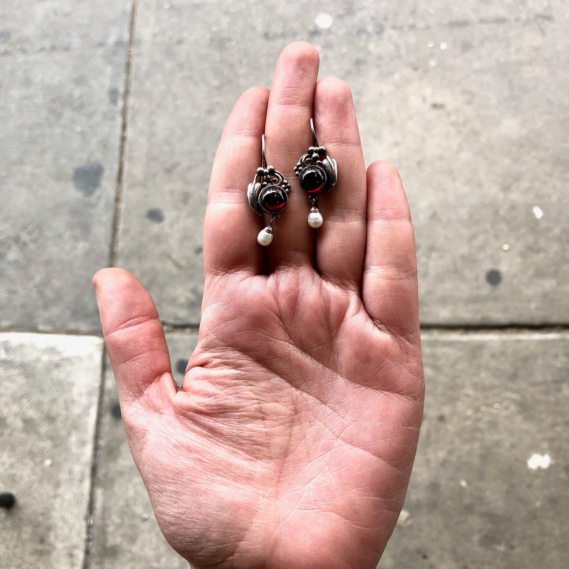 Vintage silver and gemstone earrings held in an open palm on concrete background