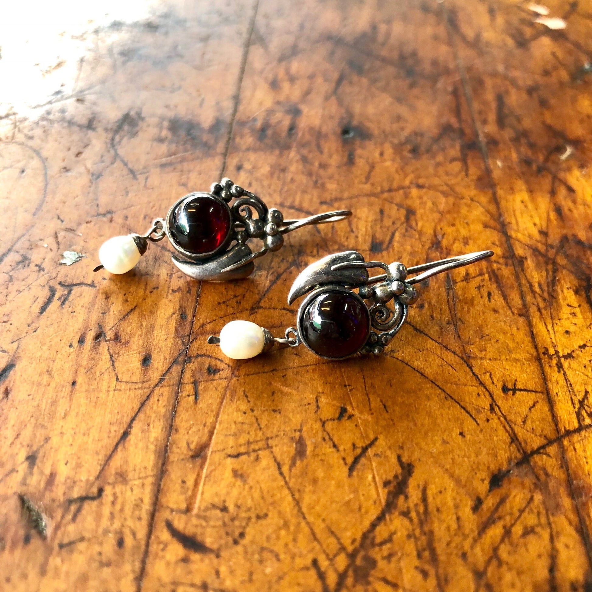 Vintage sterling silver dangle earrings with red gemstone and pearl accents on a distressed wooden surface.