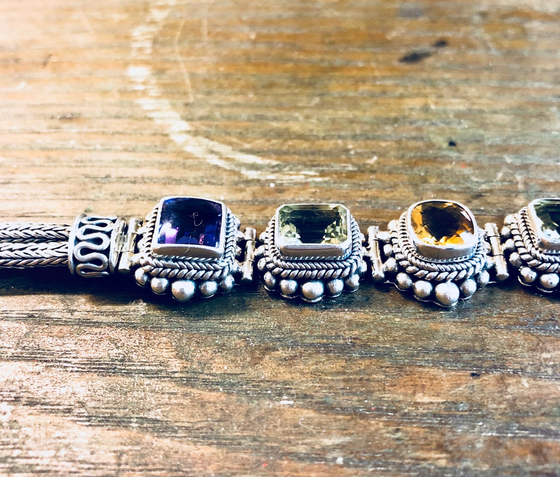 Vintage sterling silver Suarti BA gemstone link bracelet with amethyst, peridot and citrine stones in purple, green and yellow on a weathered wooden surface.