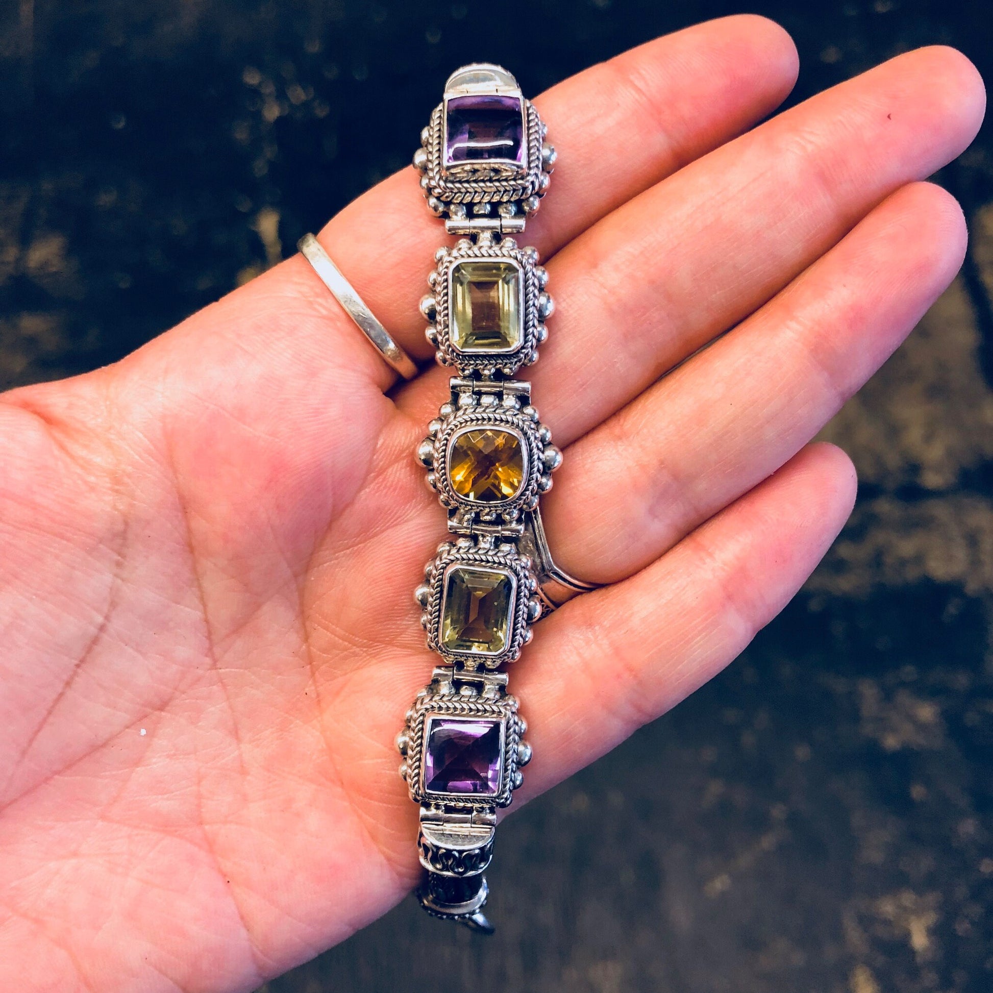 Sterling silver vintage-style bracelet featuring amethyst, peridot and citrine gemstones in an ornate link design, held in a person's palm.