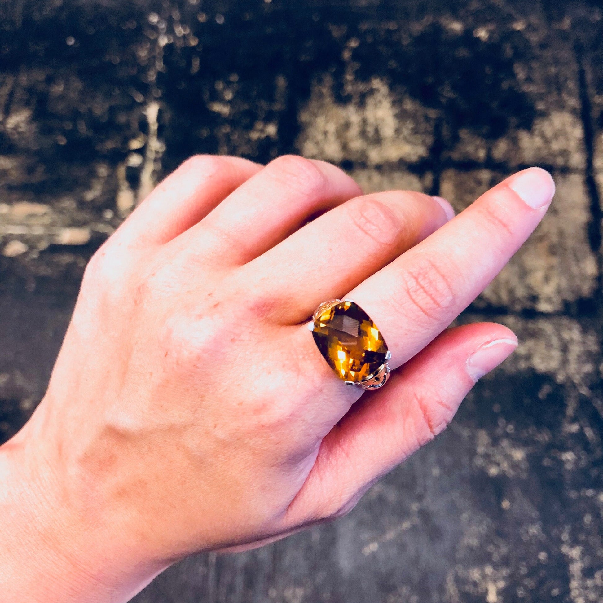 Vintage sterling silver cocktail ring with oval-cut topaz or cubic zirconia gemstone, worn on a hand against a textured dark background.