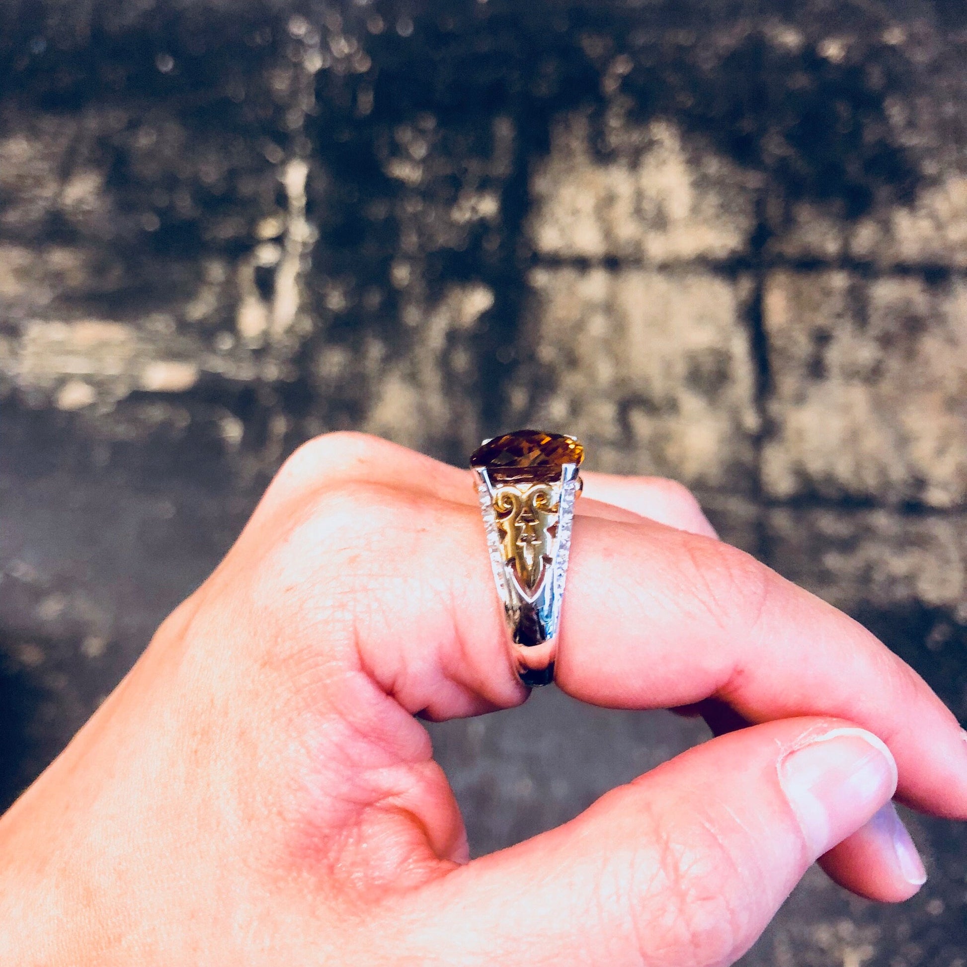 Vintage sterling silver cocktail ring with topaz-colored cubic zirconia stone, held in hand against textured background